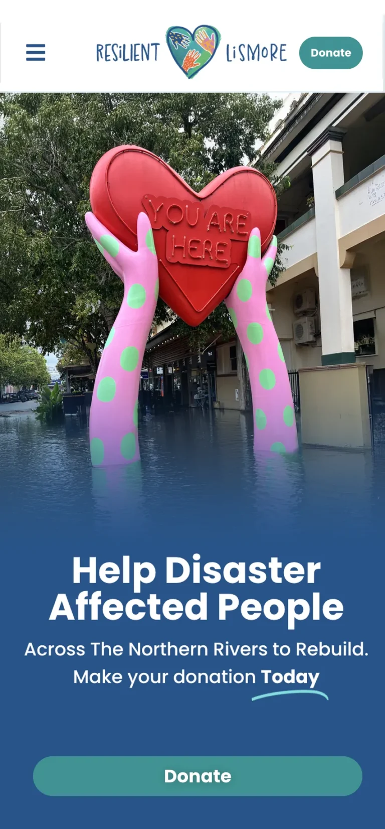 You are here heart statue surrounded by flood water. Text reads:Help Disaster Affected People Across The Northern Rivers to Rebuild. Make your donation Today.